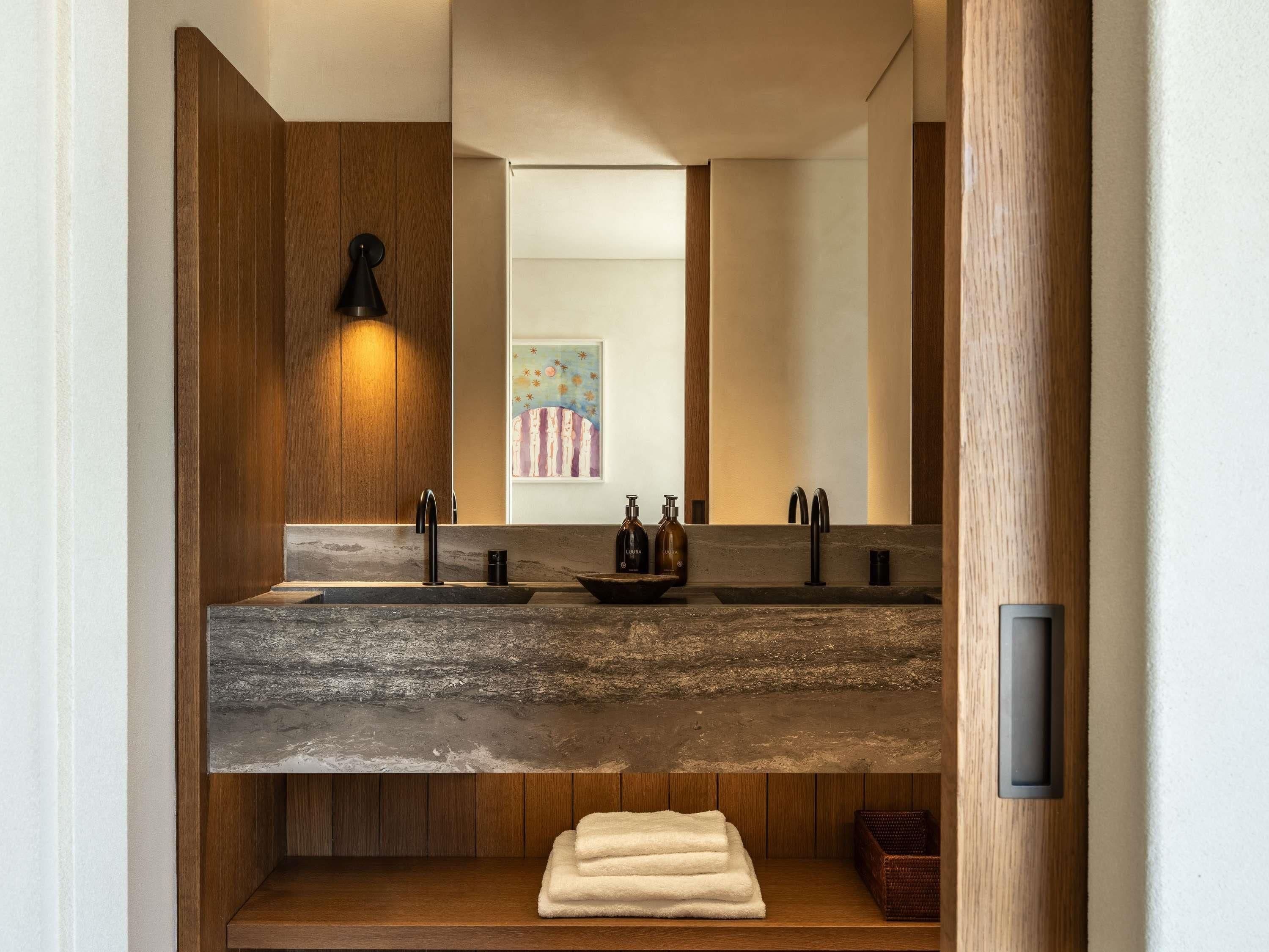 A modern bathroom with a stone countertop, wooden paneling, a large mirror, and a towel rack.