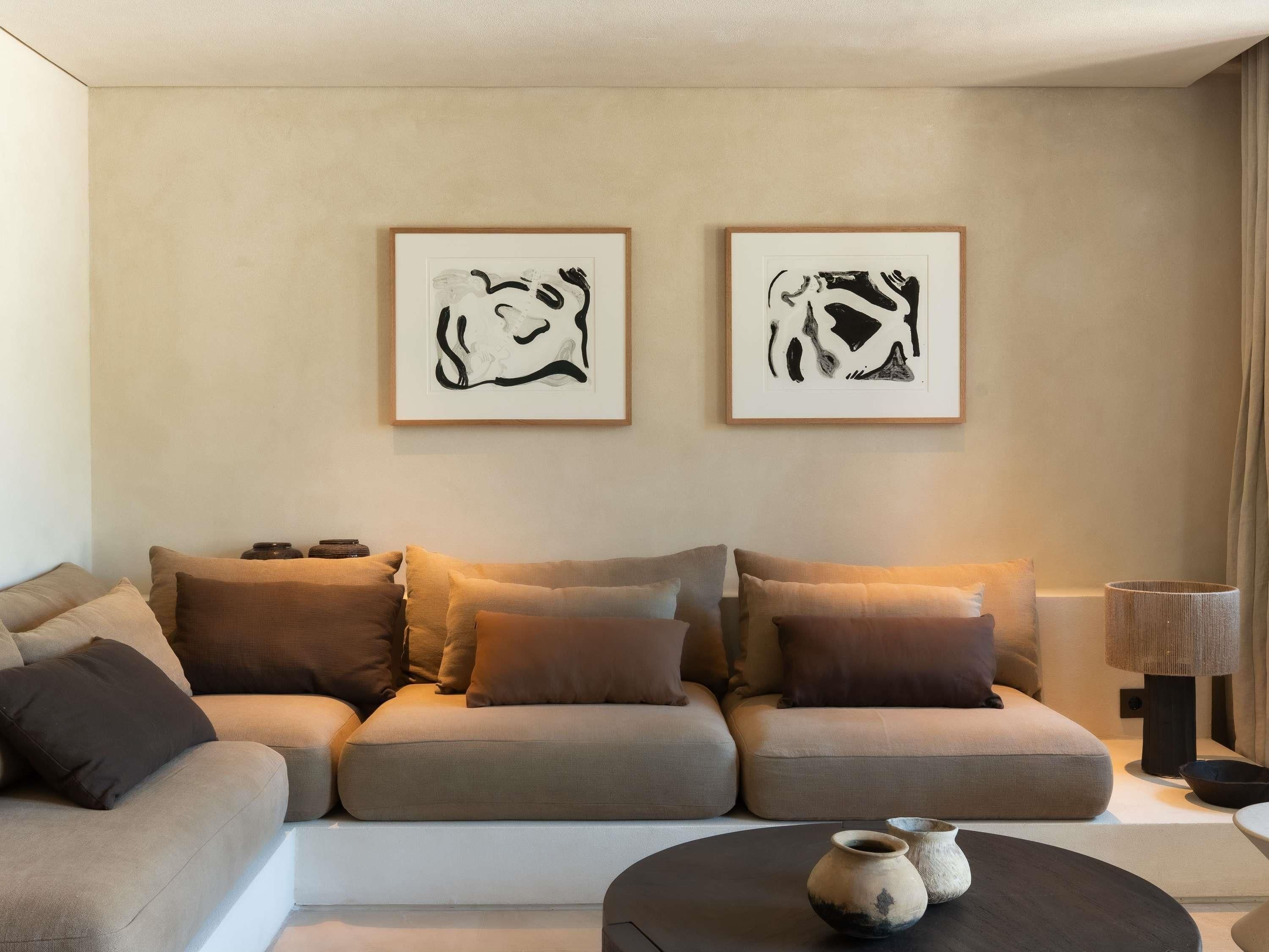 A modern living room with a sofa set, two framed abstract artworks, a round coffee table with decorative items, and a floor lamp.