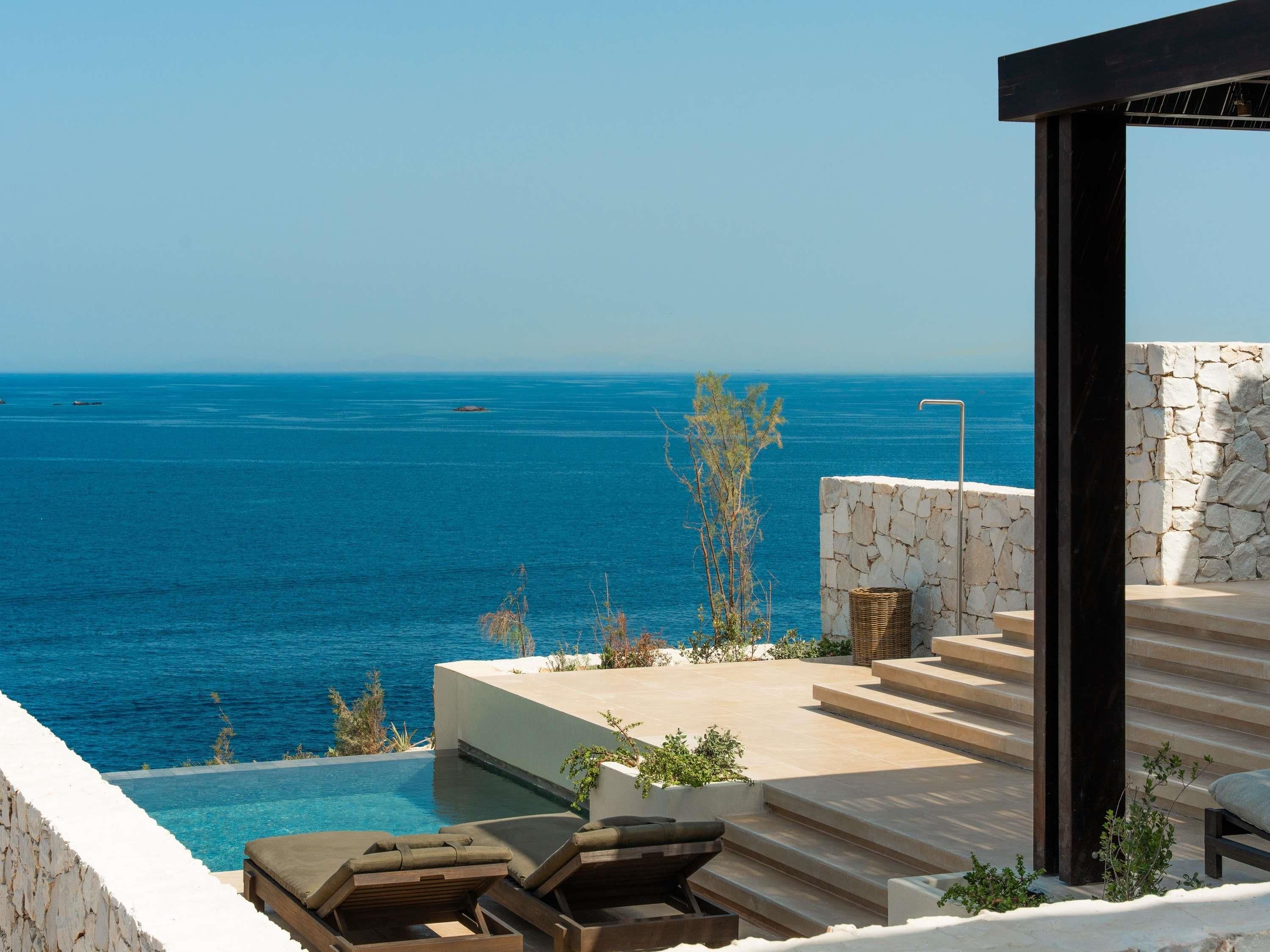 Un espace aménagé au bord de la piscine, avec vue sur la mer, des murs en pierre et des sièges d’extérieur.