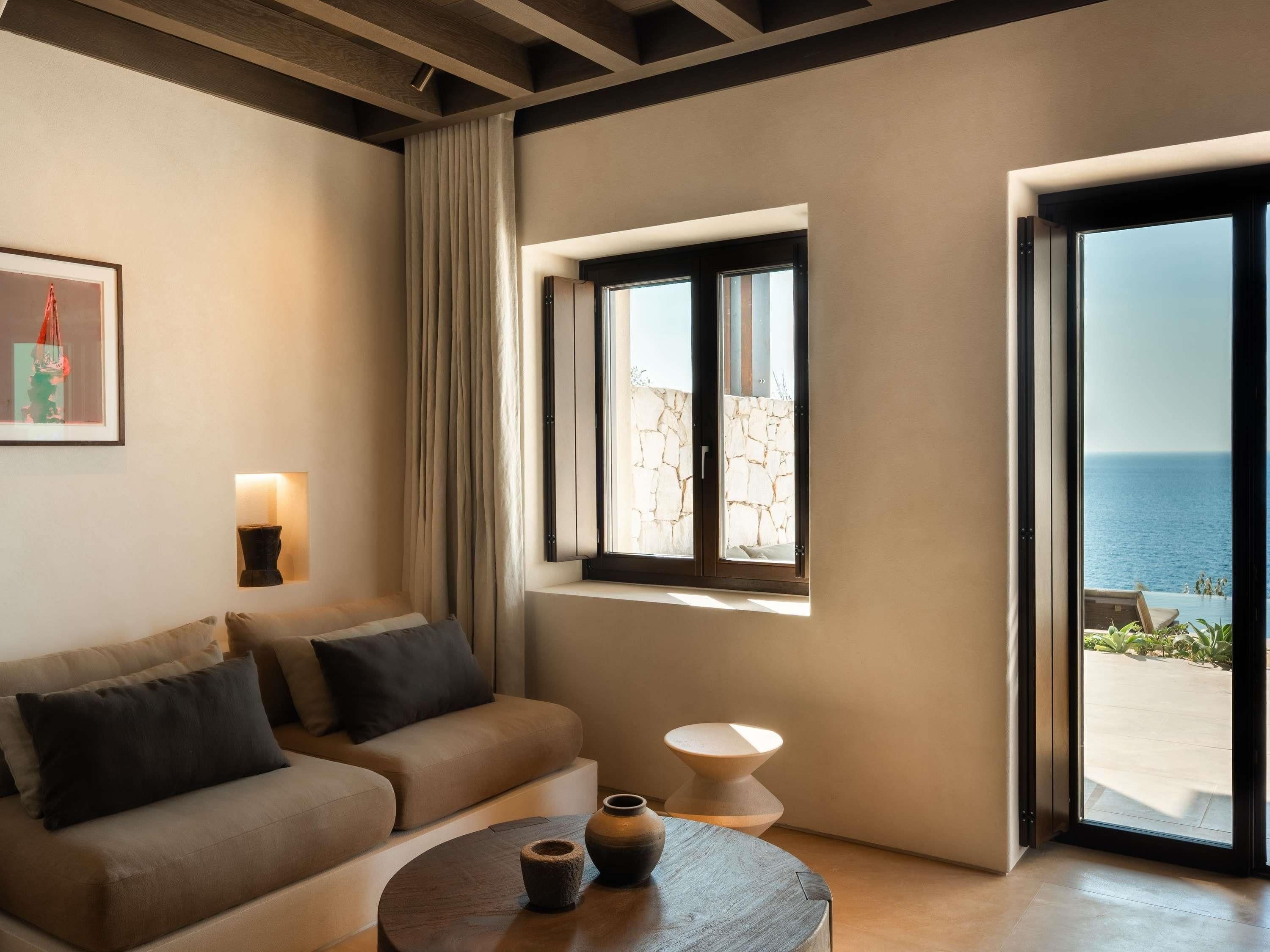 Una sala de estar moderna con un sofá, una mesa de centro, una ventana con vista al mar y un cuadro en la pared.