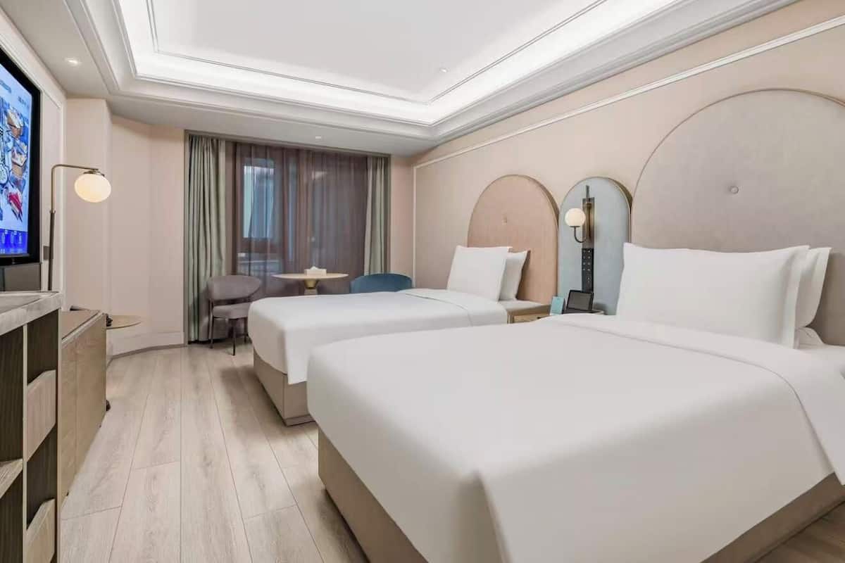 Ein Hotelzimmer mit zwei Betten, einem Fernseher, einem Schreibtisch und einem Sessel.