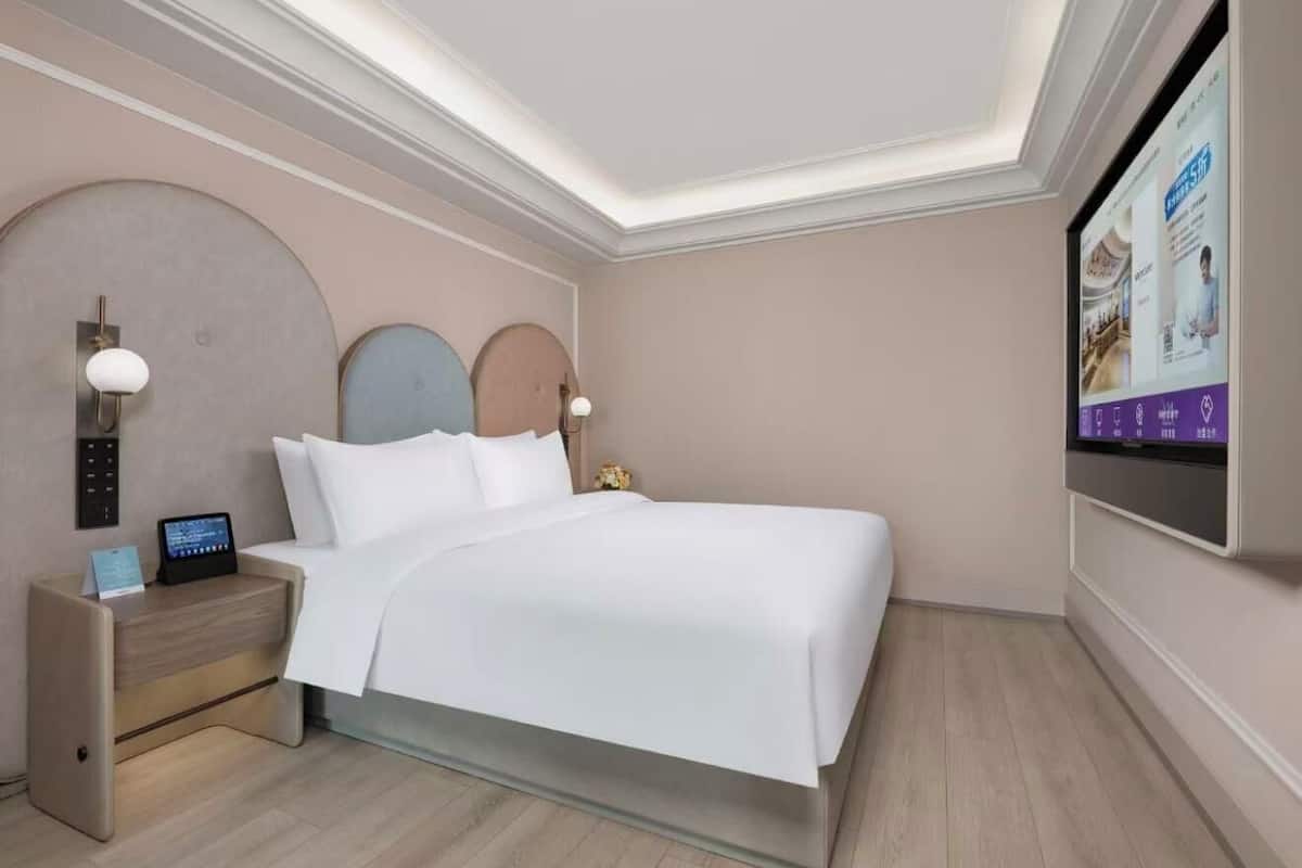 Ein modernes Hotelzimmer mit Bett, Nachttischen, Fernseher und Deckenleuchte.