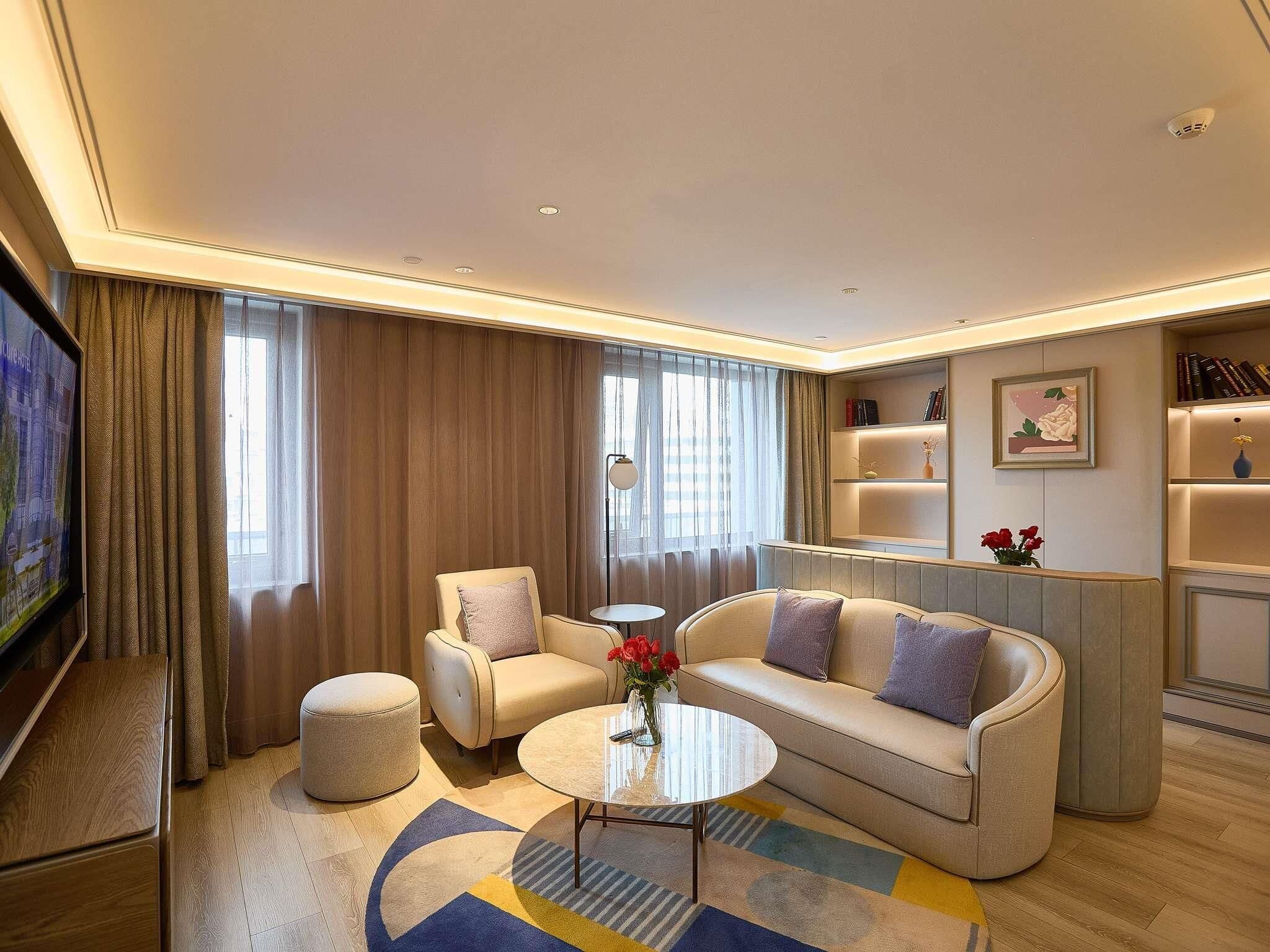 Una habitación de hotel moderna con sofá, sillones, una mesa de centro y televisor.