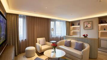 Una habitación de hotel moderna con sofá, sillones, una mesa de centro y televisor.