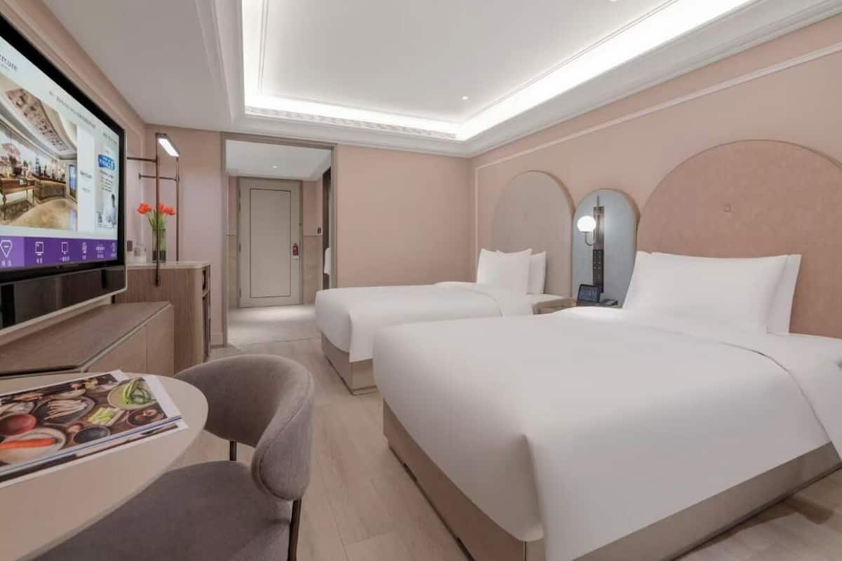 Ein Hotelzimmer mit zwei Betten, einem Schreibtisch mit Stuhl, einem Fernseher und einem Spiegel.