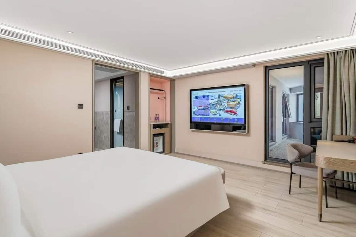 Ein Hotelzimmer mit einem Bett, einem Schreibtisch, einem Fernseher und einer Schiebetür, die auf einen Balkon führt.
