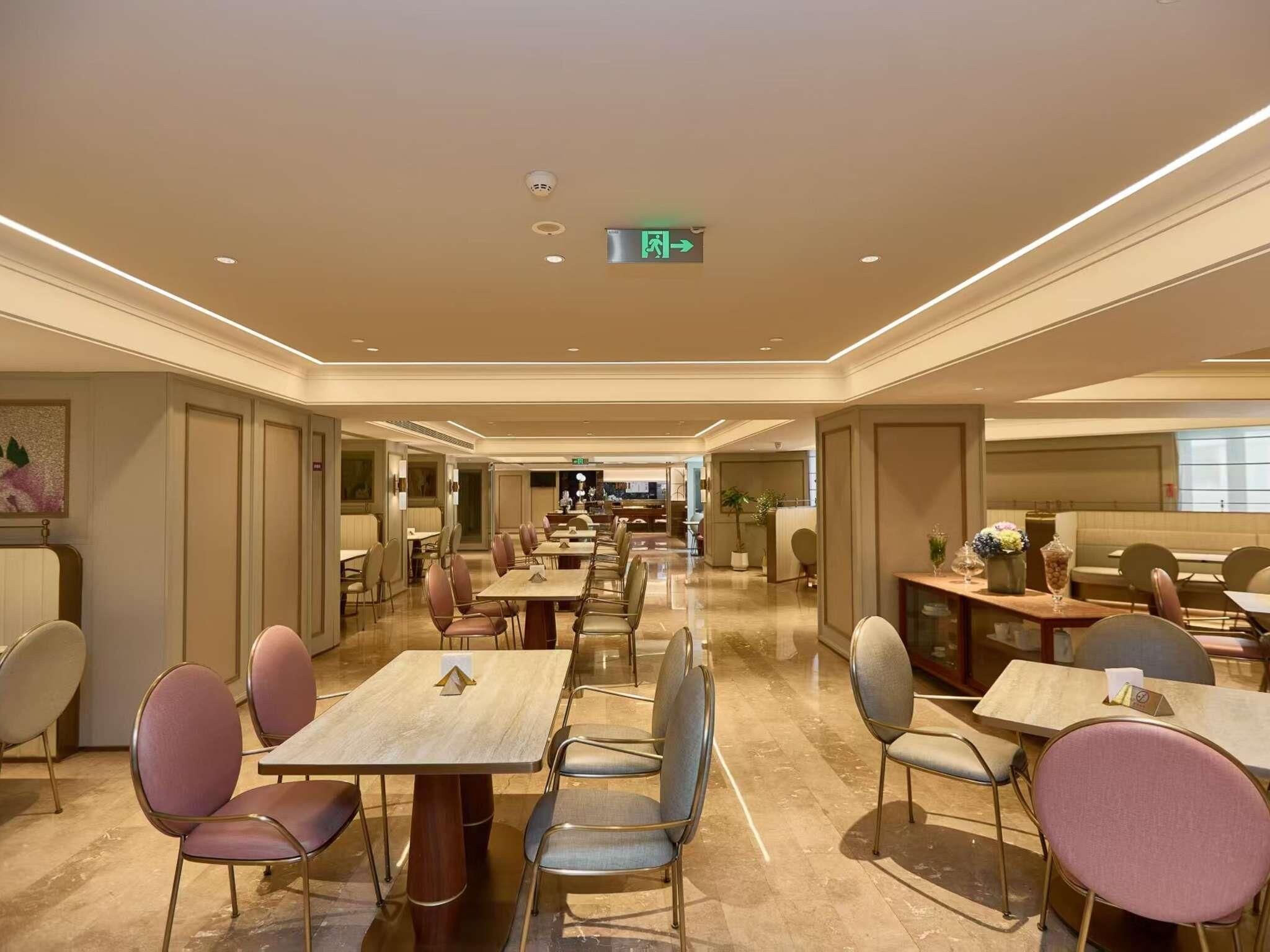 Un comedor amplio de hotel con varias mesas y sillas, un letrero de salida visible y un interior moderno y limpio.