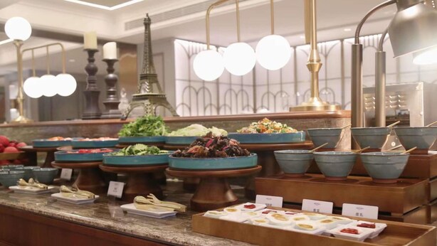 Un'impostazione per buffet con diversi piatti e ciotole, una Torre Eiffel decorativa e un lampadario moderno.