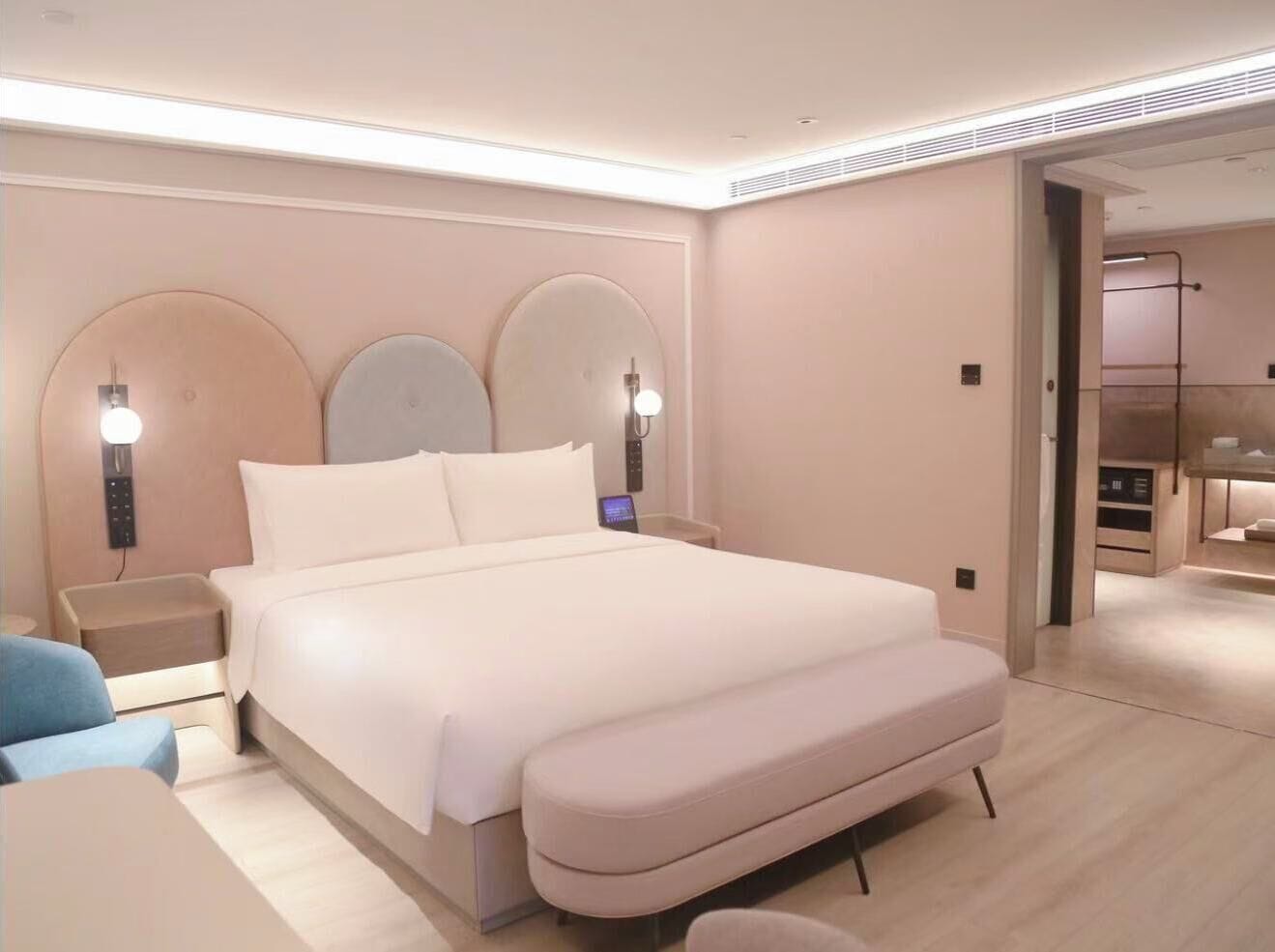 A modern bedroom with a large bed, bedside lamps, a nightstand, and a small seating area.