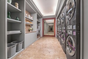 A laundry room with multiple washing machines, shelves with laundry supplies, and baskets.