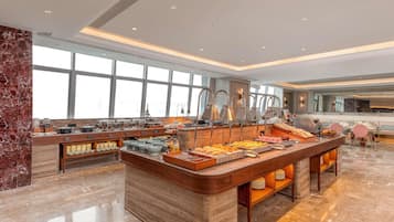 Un vaste espace dédié au petit-déjeuner à l’hôtel, doté d’un comptoir en marbre, de plusieurs buffets et de grandes fenêtres laissant entrer la lumière naturelle.