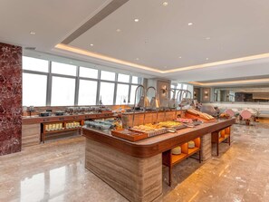 Un vaste espace dédié au petit-déjeuner à l’hôtel, doté d  ’un comptoir en marbre, de plusieurs buffets et de grandes fenêtres laissant entrer la lumière naturelle.