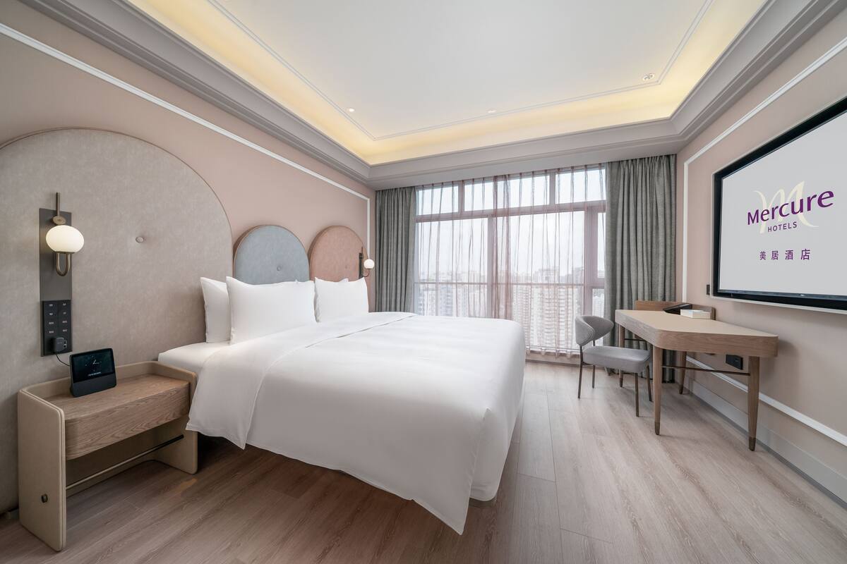 A hotel room with a bed, desk, and a large window.