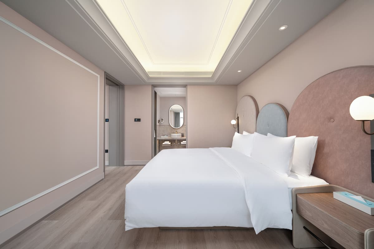 A modern hotel room with a large bed, a bedside table, a mirror, and a round wall clock.