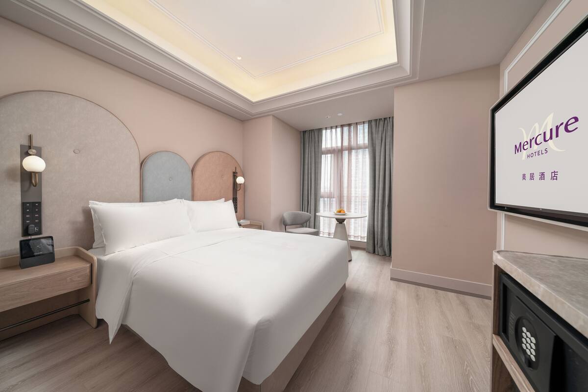 A hotel room with a bed, bedside table, lamp, and a television screen displaying the hotel name.