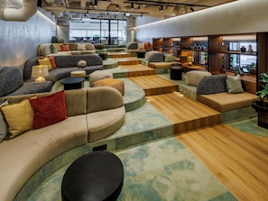 A modern lounge area with curved sofas, wooden tables, and a view of the outdoors. - Novotel Tallinn (Tallinn)