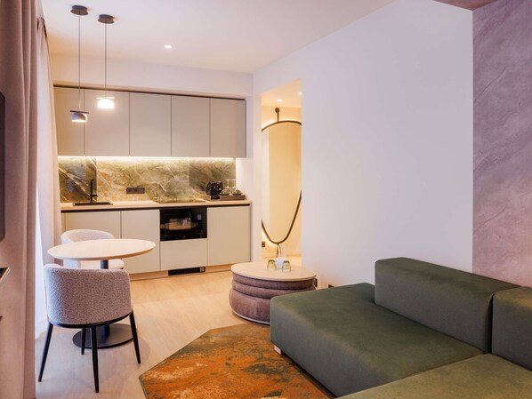 Een moderne woonkamer met een groene bank, een ronde salontafel en een eethoek met een witte tafel en stoelen.