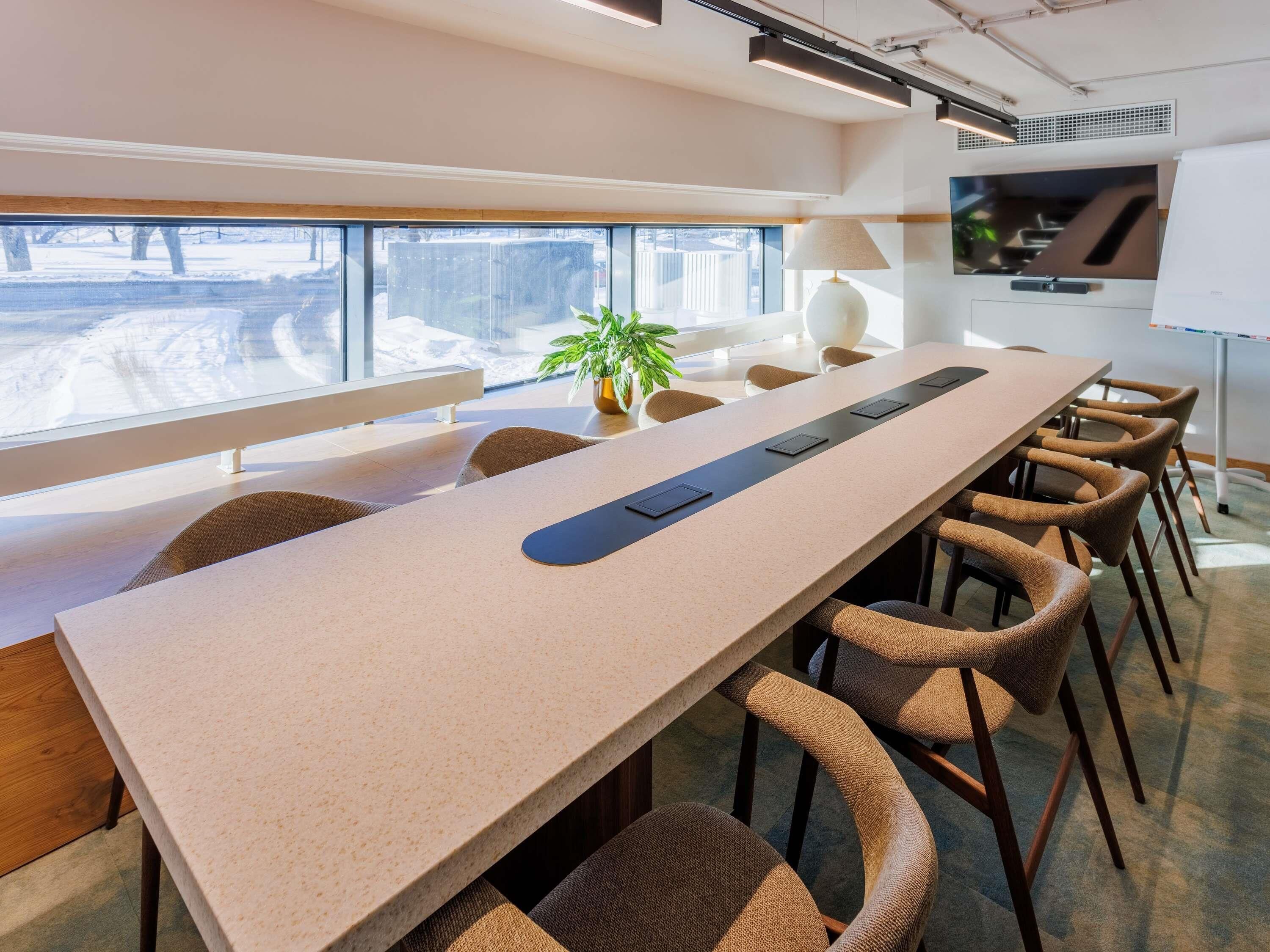 A conference room with a long table, chairs, a plant, and a view of a snowy landscape through large windows.