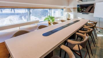 A conference room with a long table, chairs, a plant, and a view of a snowy landscape through large windows.