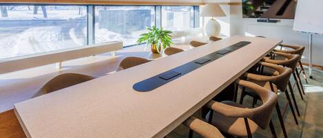 A conference room with a long table, chairs, a plant, and a view of a snowy landscape through large windows.