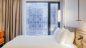 Une chambre d’hôtel avec un grand lit, une chaise, une table de chevet et une vue sur les immeubles par la fenêtre.
