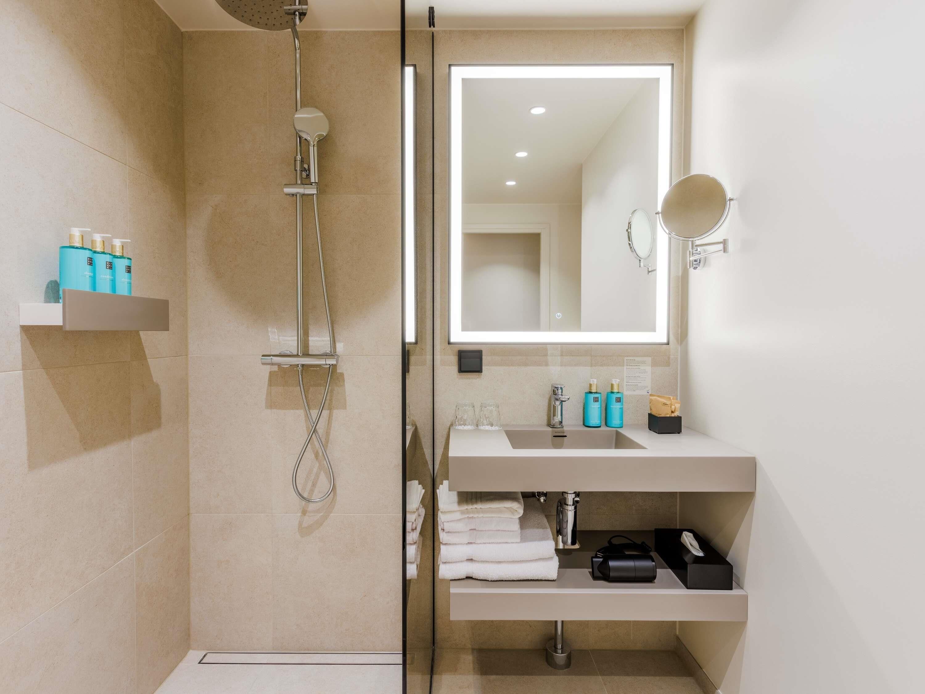 A modern bathroom with a glass-enclosed shower, a large mirror, and a vanity with toiletries.