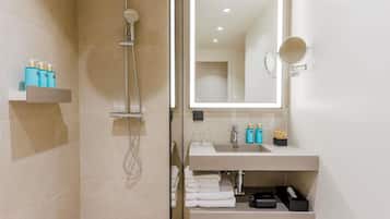 A modern bathroom with a glass-enclosed shower, a large mirror, and a vanity with toiletries.