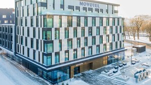 Un hôtel moderne, avec une façade en verre, portant l’inscription « NOVOTEL », qui se distingue par son architecture symétrique et son entrée centrale.