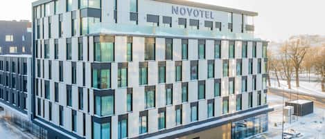 A modern hotel building with a glass facade, labeled 'NOVOTEL,' featuring a symmetrical design and a central entrance.