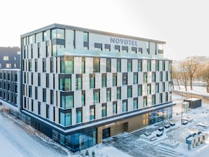 A modern hotel building with a glass facade, labeled 'NOVOTEL,' featuring a symmetrical design and a central entrance.