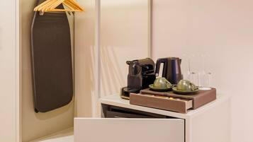 A hotel room with a bed, a hanging garment, a coffee maker, a kettle, and a tray with cups and glasses.