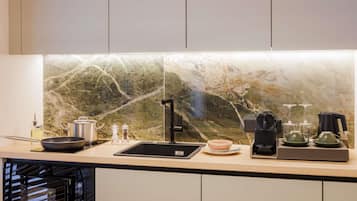 Une cuisine moderne avec un dosseret en marbre, un robinet noir, une machine à café et une bouilloire posées sur le plan de travail.