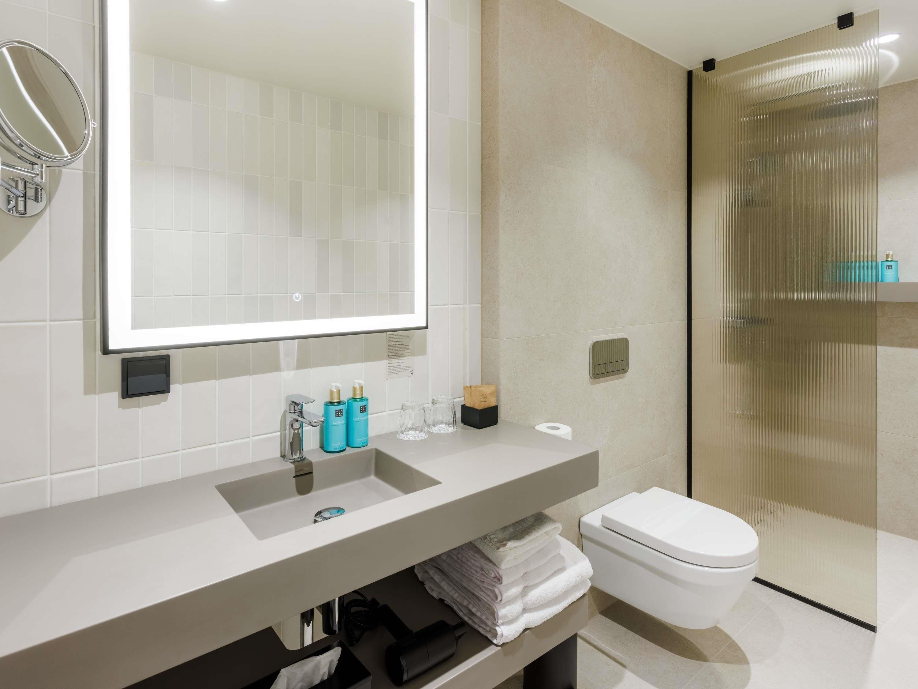 A modern bathroom with a large mirror, a sink, a toilet, and a glass shower enclosure.