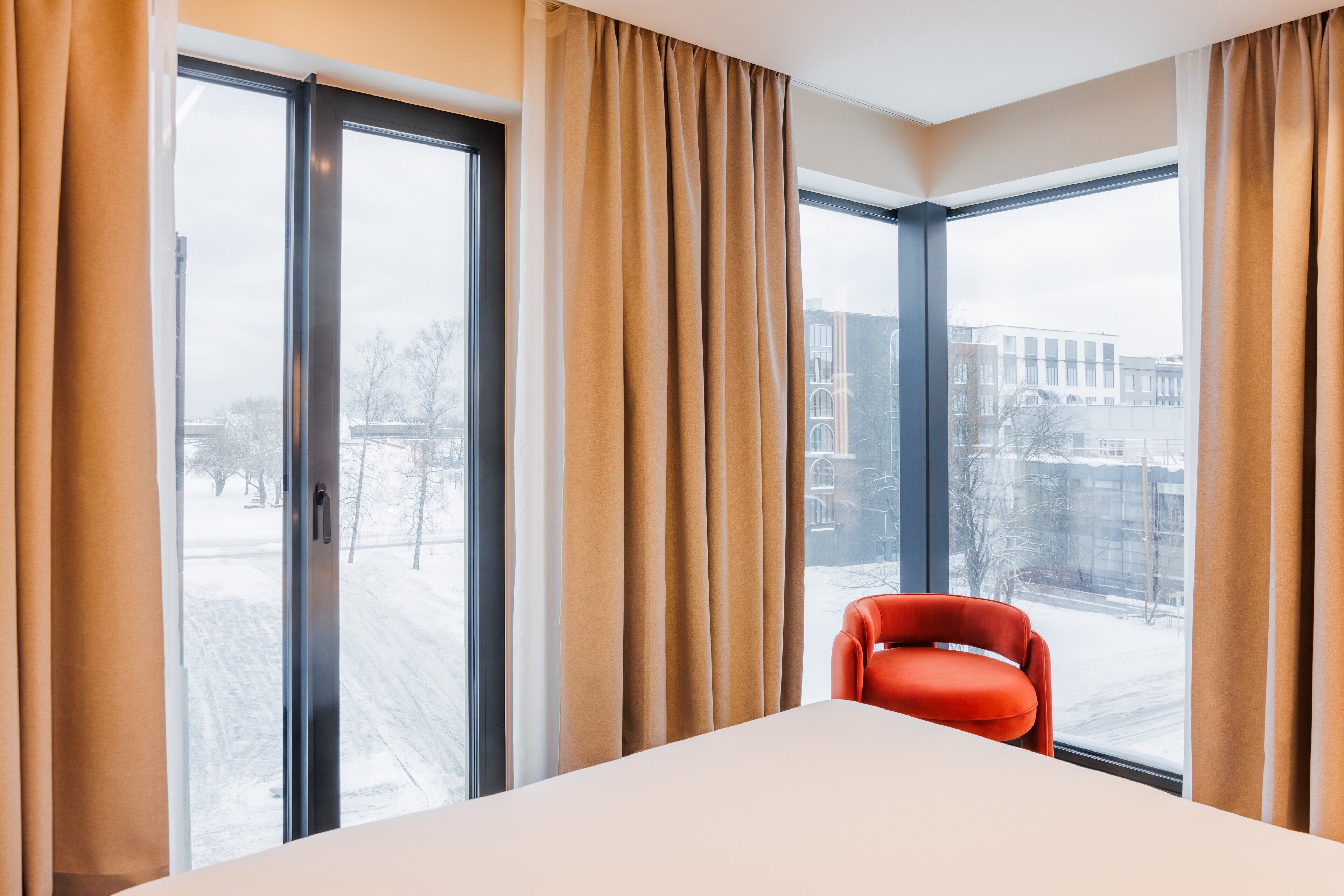 Habitació d'hotel amb grans finestres, un llit i una cadira vermella.