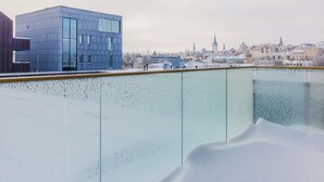Un bâtiment moderne doté de grandes fenêtres, d’une balustrade en verre et, en arrière-plan, d’un paysage urbain enneigé.