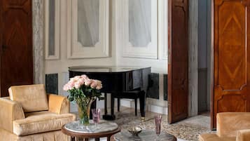 Una sala amplia con un piano, dos sofás y una mesa de centro de mármol con un jarrón de flores.