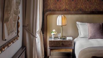 A hotel room with a bed, a nightstand, a lamp, a vase with flowers, and a wall with a patterned wallpaper.