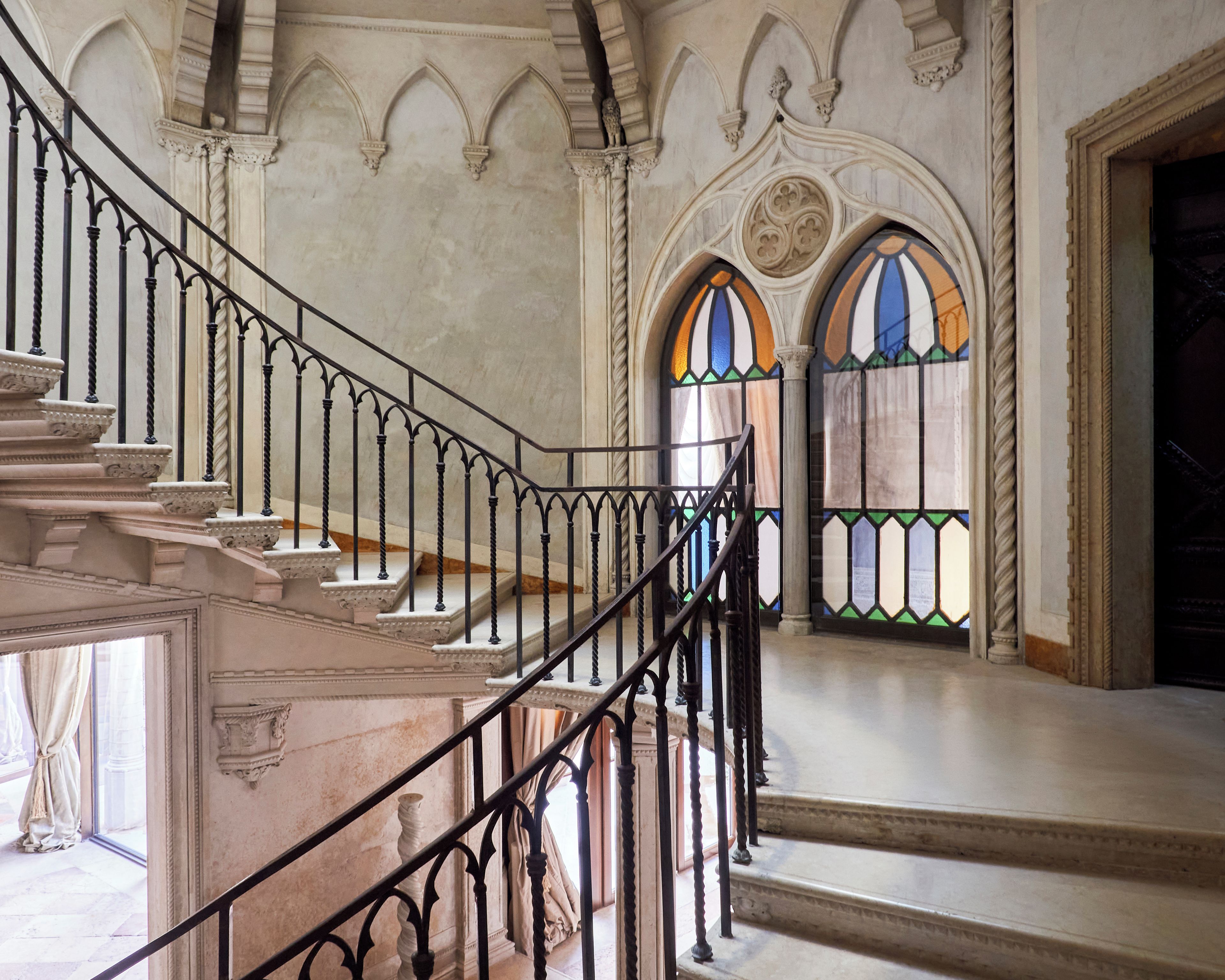 A grand staircase with ornate balustrades leading to a high ceiling with decorative moldings.