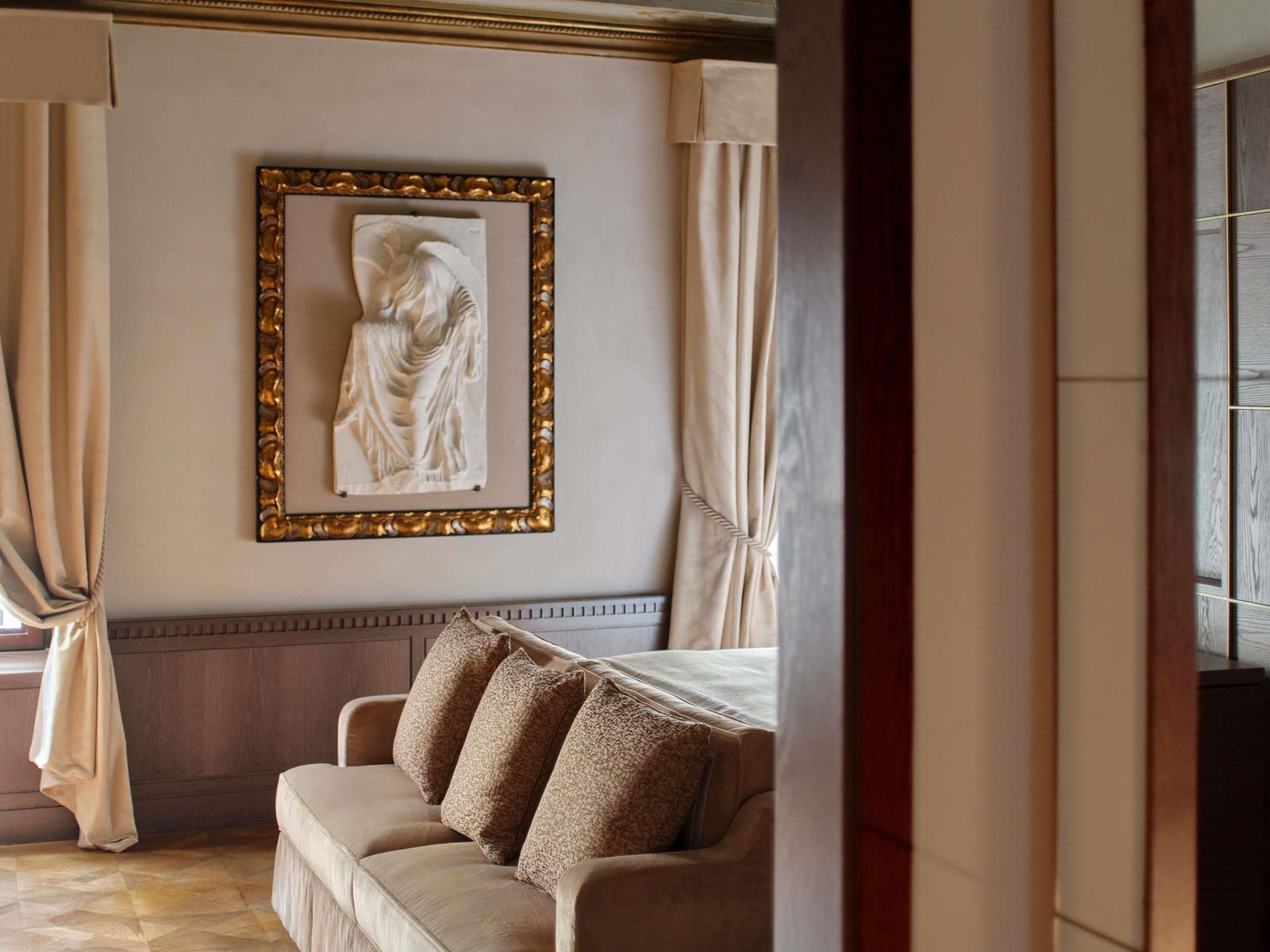 A room with a beige sofa, a framed artwork on the wall, and a window with curtains.