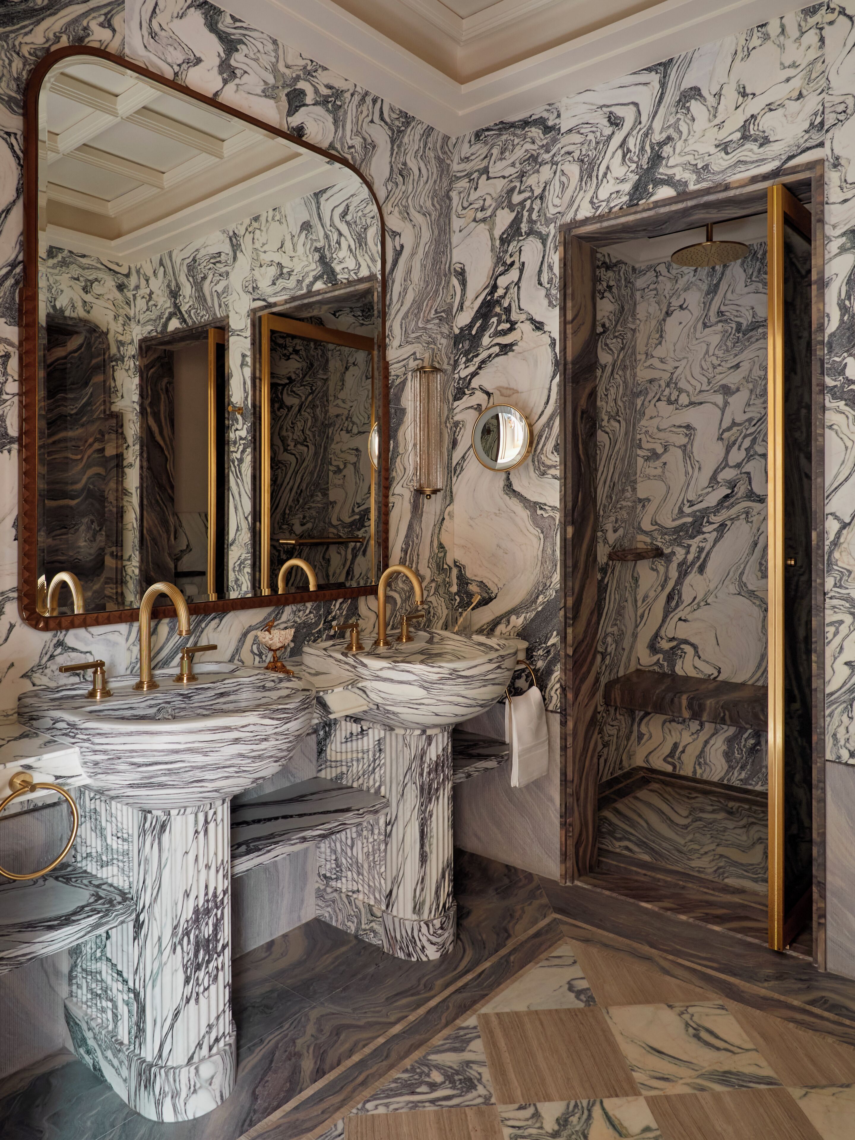 Ein Badezimmer mit Marmorwänden, einem großen Spiegel und zwei Waschbecken mit goldfarbenen Armaturen.