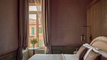 Une chambre d’hôtel avec un lit, une petite table, un vase avec des fleurs, une lampe et une vue sur les bâtiments à l’extérieur de la fenêtre.