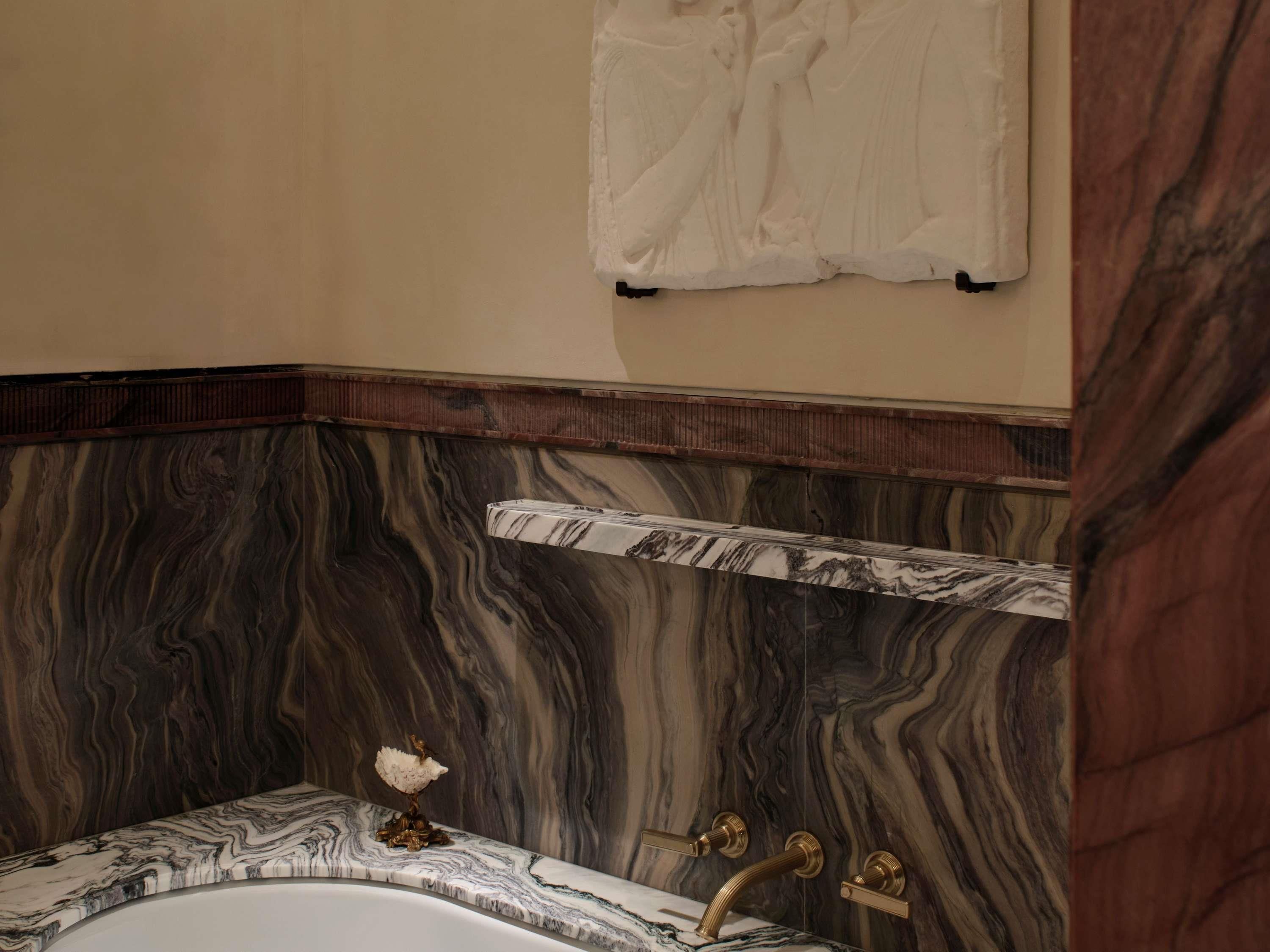 Une salle de bain avec un lavabo en marbre, un robinet doré et un mur en marbre.