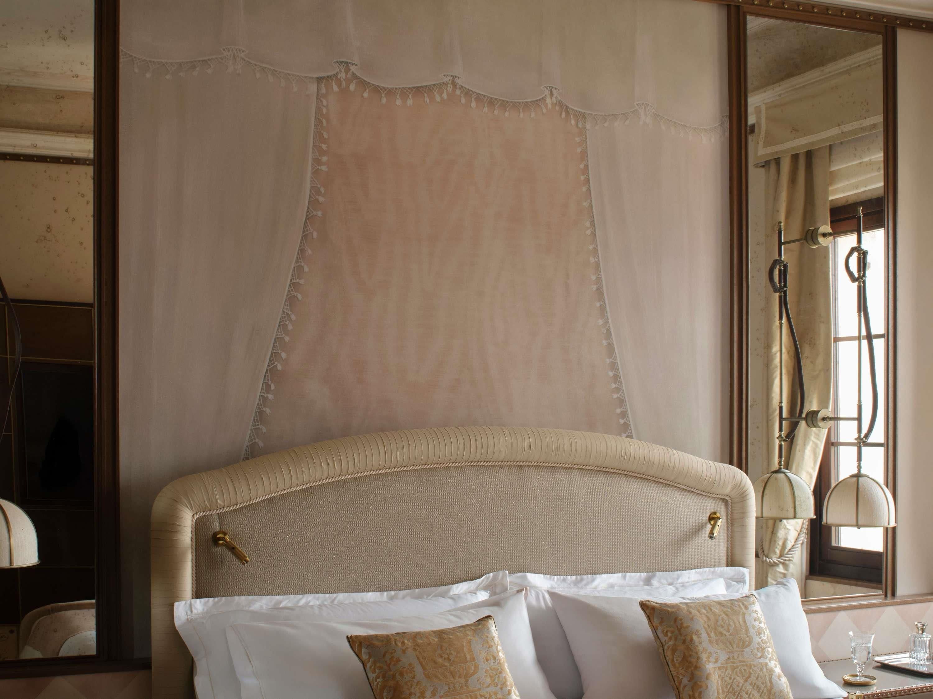 Une chambre à coucher avec un grand lit, un miroir et une fenêtre avec des rideaux.