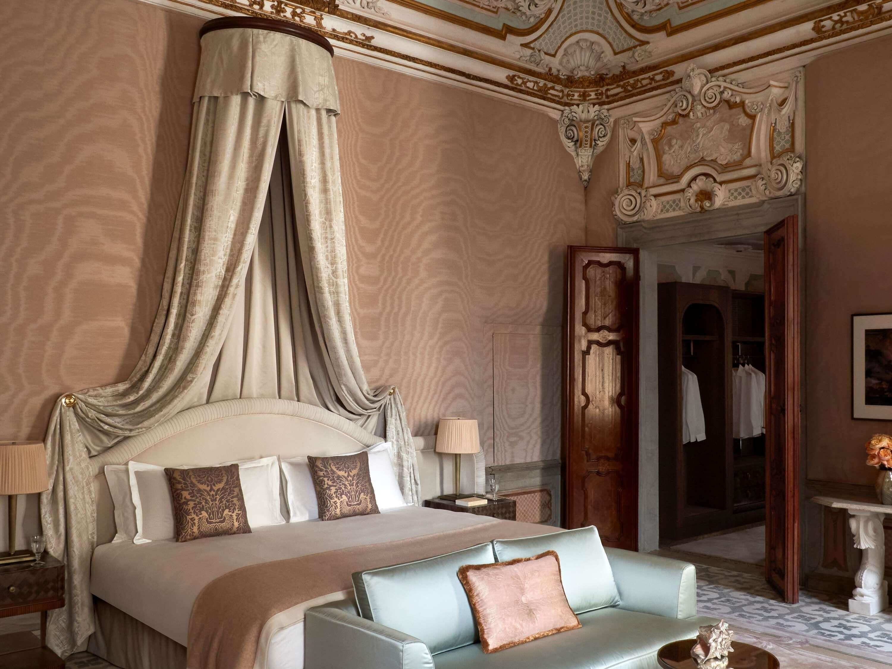 A luxurious bedroom with a canopy bed, a chaise lounge, and ornate ceiling decorations.