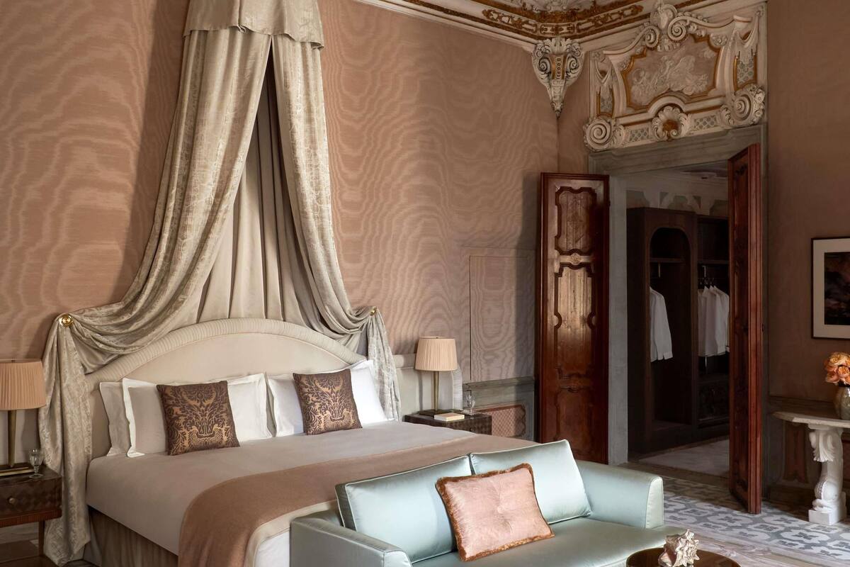 A luxurious bedroom with a canopy bed, a chaise lounge, and ornate ceiling decorations.