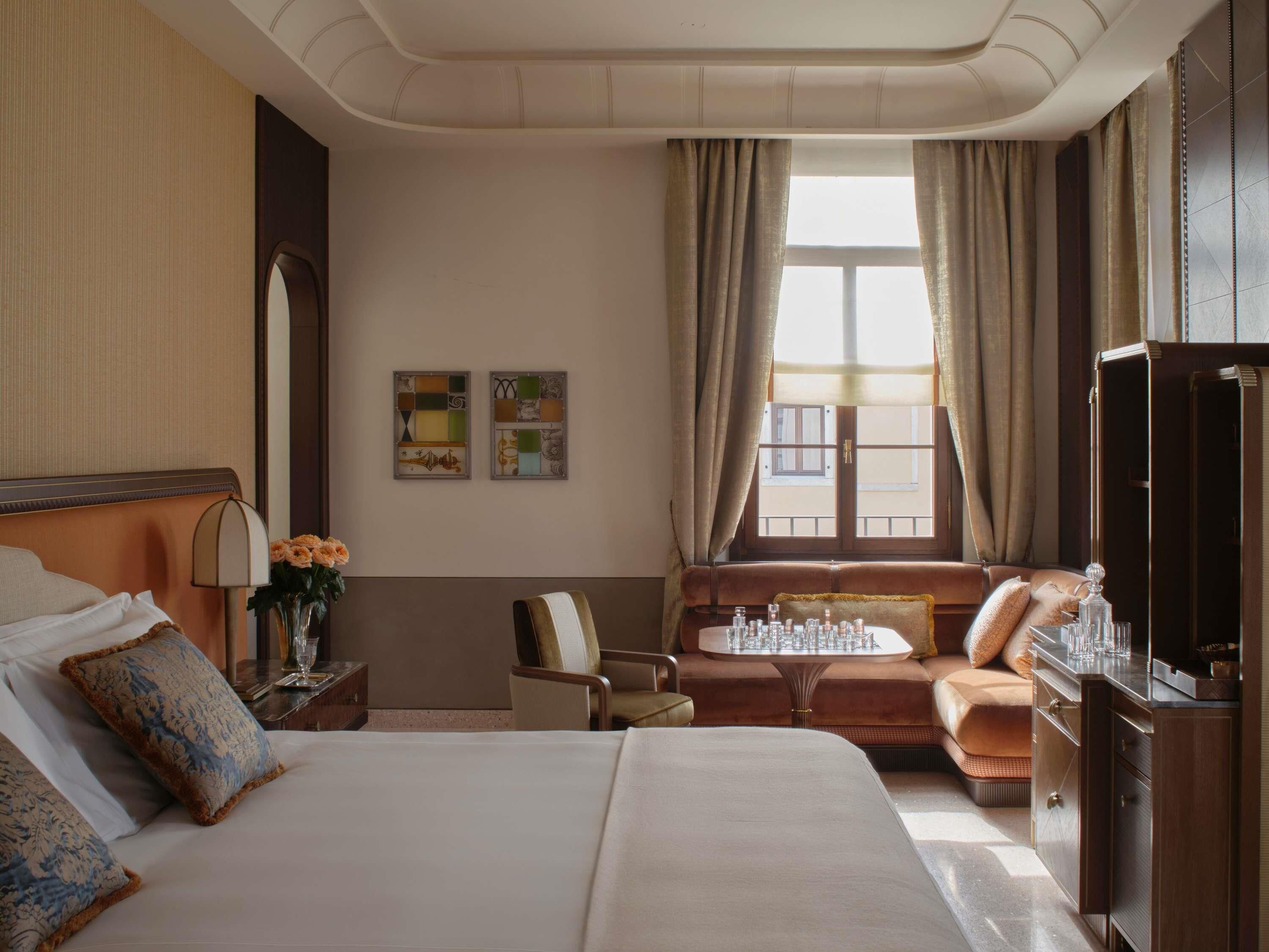 A hotel room with a large bed, a seating area with a table, a mirror, and artwork on the walls.