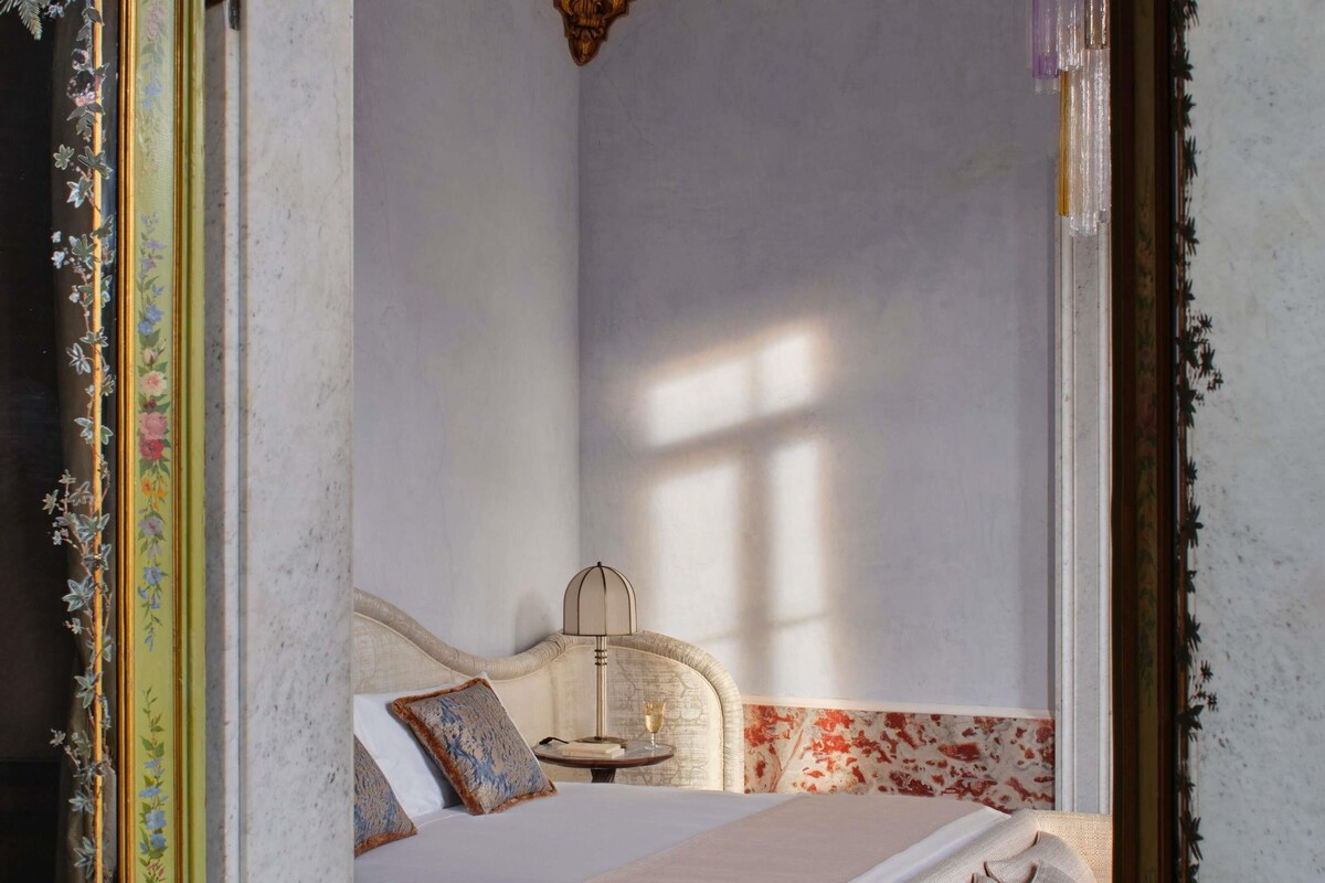 Une chambre à coucher avec un lit, des oreillers, une table de chevet avec une lampe et une fenêtre.