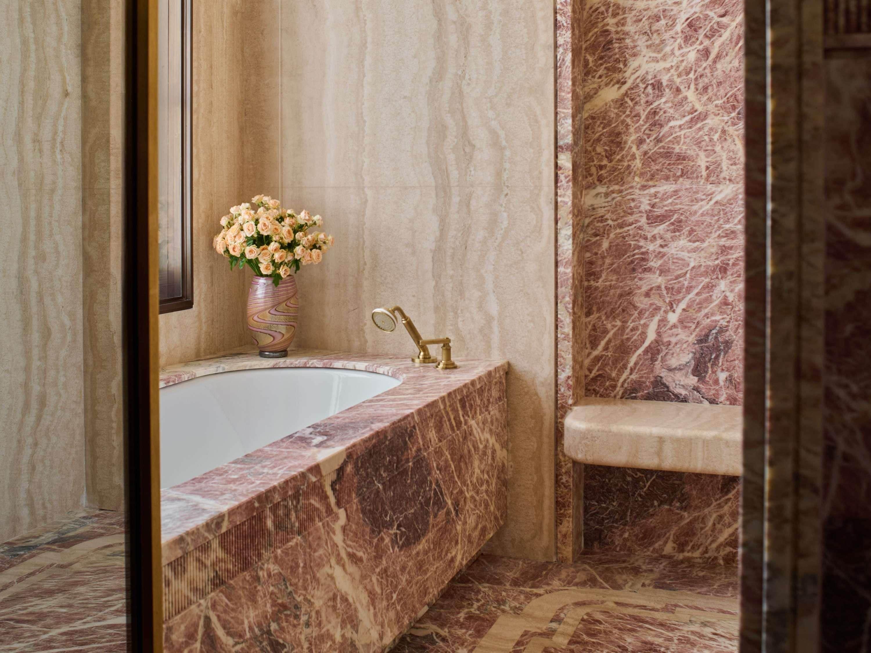 A marble bathtub with a gold faucet, a vase of flowers, and a marble bench.