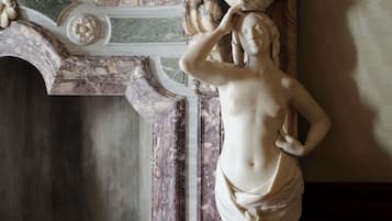A marble statue with a draped garment, set against a wall with ornate architectural details.