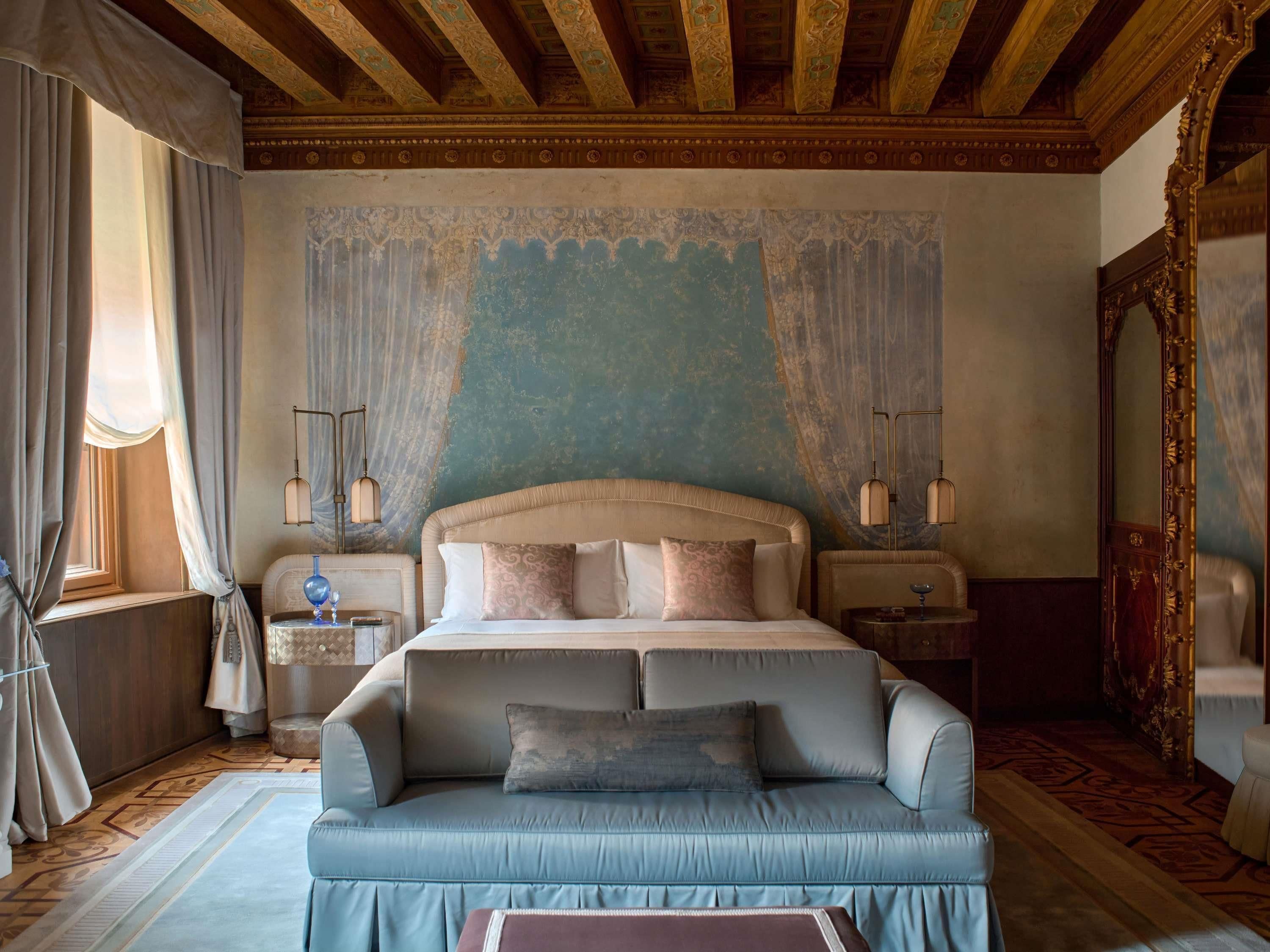 A bedroom with a large bed, a sofa, a nightstand, a mirror, and a window with curtains.